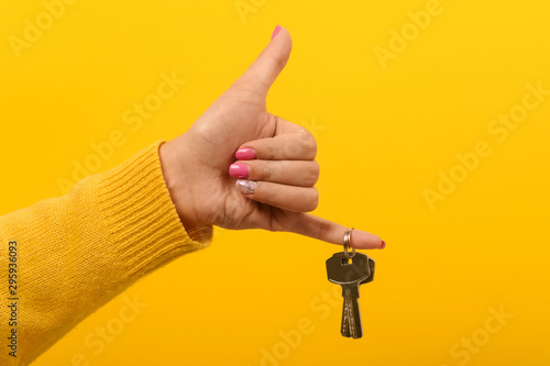 Fotomural female hand holding house keys and showing thumb up, over yellow background