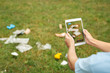 © Viktoriia - Waste Management. Young girl sitting a park holding smartphone using app for litter recognition and sorting plastic identified on screen close-up