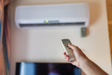 In Female Hands Of The Remote Control Air Conditioning In The Hotel Room. Cooling And Airing In The Hotel Room. Close-up View Of The Use Of Some Electrical Appliances Such As Air Conditioning.