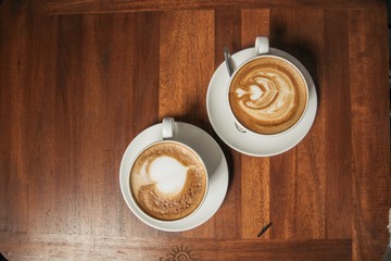 Canvas Print - High angle shot of two cups of coffee with cute hearts on a wooden table