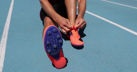 Wall Mural - Athlete sprinter getting ready to run tying up shoe laces on stadium running tracks. Man track runner preparing for cardio training outdoors. Fitness and athletics sports. Blue background.