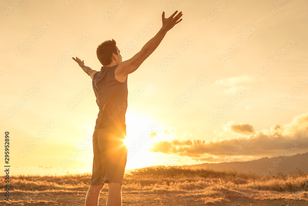 Happy man looking up to the sky with arms raised up to the sunset.  - obrazy, fototapety, plakaty 