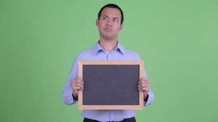 Poster - Happy Asian businessman thinking while holding blackboard