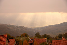 The Sun's Rays Through The Clouds Illuminate The Tiled Roofs