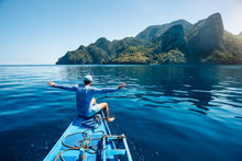 Back View Of The Man On Boat With Spreading Hands Arriving To Exotic Tropical Island Lit By Sun Light. Travelling Tour In Asia: El Nido, Palawan, Philippines