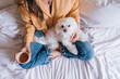 beautiful woman playing with her cute maltese dog at home. Drinking tea or coffee on bed. Relax and Lifestyle