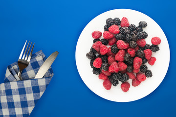  blackberry and raspberry on a white plate. blackberry and raspberries on a background top view. Vegetarian food.