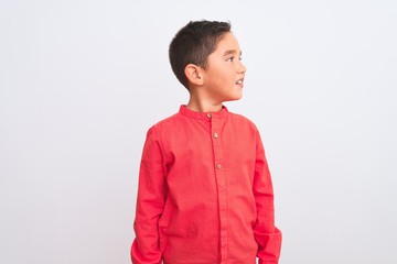 Beautiful kid boy wearing elegant red shirt standing over isolated white background looking away to side with smile on face, natural expression. Laughing confident.