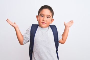 Poster - Beautiful student kid boy wearing backpack standing over isolated white background clueless and confused expression with arms and hands raised. Doubt concept.