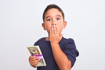 Canvas Print - Beautiful kid boy holding dollars standing over isolated white background cover mouth with hand shocked with shame for mistake, expression of fear, scared in silence, secret concept