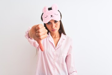 Wall Mural - Young beautiful woman wearing sleep mask and pajama over isolated white background looking unhappy and angry showing rejection and negative with thumbs down gesture. Bad expression.