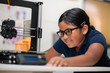 © mmg1design - A happy young girl wearing glasses and watching a 3d printer finish the 3d model she created.