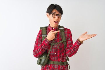 Sticker - Chinese hiker man wearing backpack canteen glasses over isolated white background amazed and smiling to the camera while presenting with hand and pointing with finger.