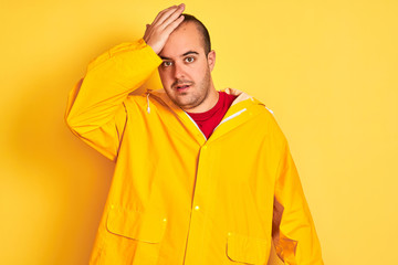 Sticker - Young man wearing rain coat standing over isolated yellow background surprised with hand on head for mistake, remember error. Forgot, bad memory concept.