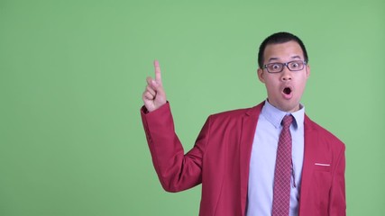 Wall Mural - Happy Asian businessman with eyeglasses pointing up and looking surprised