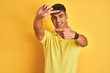 © Krakenimages.com - Young indian man wearing casual polo standing over isolated yellow background smiling making frame with hands and fingers with happy face. Creativity and photography concept.