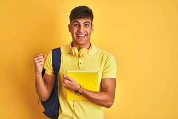 Indian student man wearing backpack headphones notebook over isolated yellow background screaming proud and celebrating victory and success very excited, cheering emotion