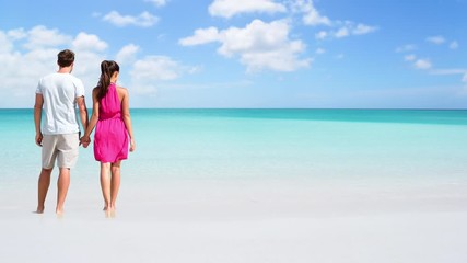 Wall Mural - CINEMAGRAPH - seamless loop: Beach couple looking at ocean view from behind. Unrecognizable couple standing on sand in dress and shorts holding hands relaxing on summer travel vacation destination.