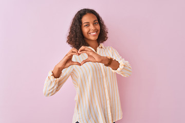 Wall Mural - Young brazilian woman wearing striped shirt standing over isolated pink background smiling in love doing heart symbol shape with hands. Romantic concept.