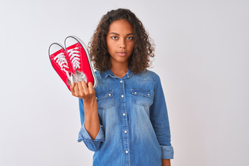 Canvas Print - Young brazilian woman holding sneakers standing over isolated white background with a confident expression on smart face thinking serious