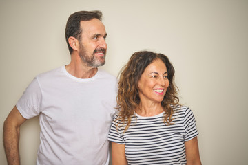 Beautiful middle age couple together standing over isolated white background looking away to side with smile on face, natural expression. Laughing confident.