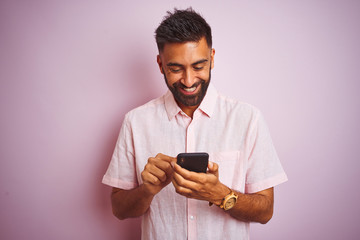 Young indian man using smartphone standing over isolated pink background with a happy face standing and smiling with a confident smile showing teeth