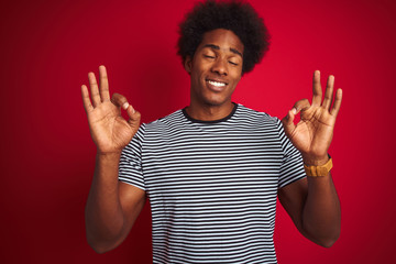 Sticker - Young american man with afro hair wearing navy striped t-shirt over isolated red background relax and smiling with eyes closed doing meditation gesture with fingers. Yoga concept.