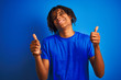 © Krakenimages.com - Afro american man with dreadlocks wearing t-shirt standing over isolated blue background success sign doing positive gesture with hand, thumbs up smiling and happy. Cheerful expression