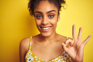 Young african american woman wearing summer floral dress over isolated yellow background doing ok sign with fingers, excellent symbol