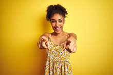 African American Woman Wearing Casual Floral Dress Standing Over Isolated Yellow Background Pointing To You And The Camera With Fingers, Smiling Positive And Cheerful