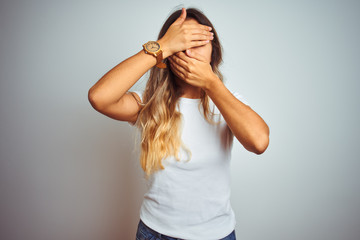 Poster - Young beautiful woman wearing casual white t-shirt over isolated background Covering eyes and mouth with hands, surprised and shocked. Hiding emotion