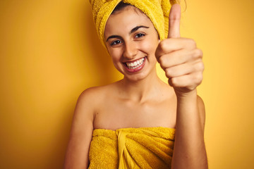 Poster - Young beautiful woman wearing a towel over yellow isolated background happy with big smile doing ok sign, thumb up with fingers, excellent sign