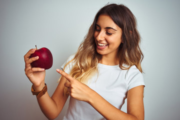 Sticker - Young beautiful woman eating red apple over grey isolated background very happy pointing with hand and finger