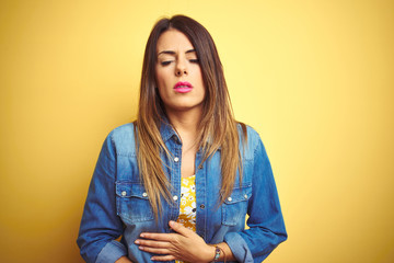 Sticker - Young beautiful woman standing over yellow isolated background with hand on stomach because indigestion, painful illness feeling unwell. Ache concept.