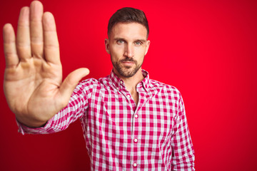 Sticker - Young handsome man over red isolated background doing stop sing with palm of the hand. Warning expression with negative and serious gesture on the face.