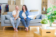 © Krakenimages.com - Young couple sitting on the sofa arround cardboard boxes moving to a new house touching mouth with hand with painful expression because of toothache or dental illness on teeth. Dentist concept.