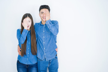 Sticker - Beautiful young asian couple over white isolated background covering one eye with hand, confident smile on face and surprise emotion.