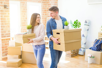 Poster - Beautiful young couple smiling in love holding cardboard boxes, happy for moving to a new home