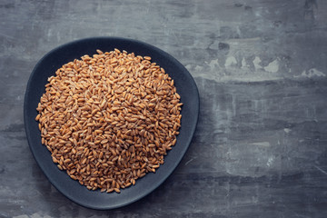 Poster - uncooked spelt on black dish on ceramic background