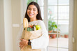© Krakenimages.com - Beautiful young woman smiling holding a paper bag full of fresh groceries at home
