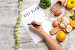 Woman writing something on sheet of paper with diet plan, top view