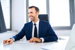 © baranq - Smiling businessman sitting in front of office computer and working