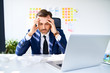 © baranq - Businessman sitting in office suffering from headache holding head in pain