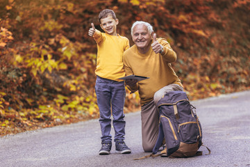 Wall Mural - Senior man with grandson in forest walk, showing thumbs up.