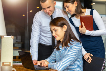 Three employees of the company look into the laptop of a colleague. the concept of business and work in a team. People work in the office. A man and two young women