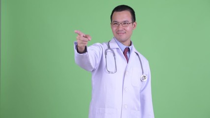 Poster - Happy Asian man doctor with eyeglasses pointing finger and directing