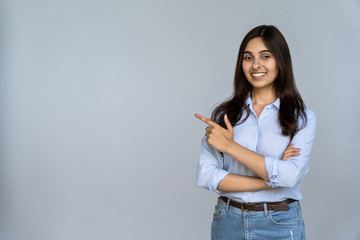 Confident smiling indian young woman professional student customer saleswoman looking at camera pointing at sales copy space isolated on grey studio background, happy lady showing aside portrait