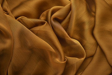 Background from silk fabric. Golden silk fabric for sewing clothes. Textural background from a transparent silk fabric.
