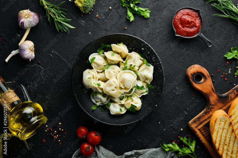 Russian pelmeni meat Dumplings with greens in a black plate. Russian traditional cuisine. Top view. Free copy space. - obrazy, fototapety, plakaty 