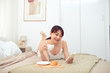 © makistock - Cheerful young Asian woman using mobile phone lying on bed in morning